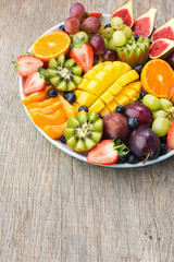 Assorted fruits and berries platter, strawberries blueberries, mango orange, apple, grapes, kiwis on the grey wood background, copy space for text, vertical, selective focus