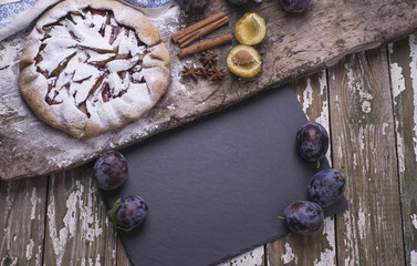 Black board for recipe of baking homemade Country Galette with plums on a wooden background.