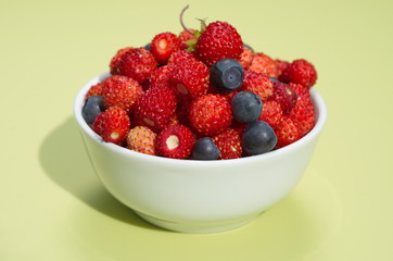 Porcelain bowl with strawberries and blueberries on yellow background