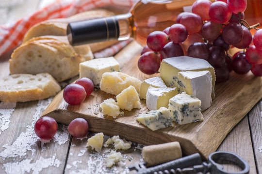 The bottle of rose wine with cheese, white bread, fresh grape on a wooden board, background.
