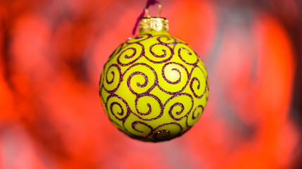 Christmas decoration or toy for Christmas tree with shimmering details. Festive decoration for Christmas tree, yellow ball with glitter decor, on red blurred background. Ornament concept