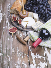 Red wine bottle with fresh grape, figs, soft figs, white bread, flowers honey on a wooden background.