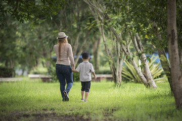 Rear view of mother and son walking together in home garden holding hand. Family concept.