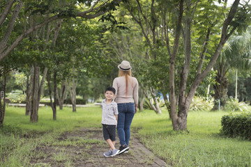 Rear view of mother and son walking together in home garden holding hand. Family concept.