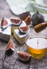 Wooden stick with flower honey, fresh figs, cheese on a wooden table.