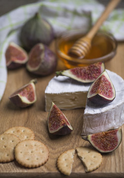 Ripe fresh figs, cheese, cracker with honey in a glass bowl on a wooden board.