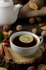 Autumn composition with hot tea on a wooden stand, cinnamon, dog rose, nuts on a brown wooden table