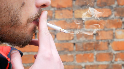 man is smoking cigarette in front of  brick wall closeup