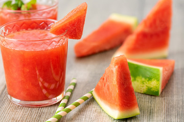 Watermelon smoothie in jars with fresh watermelon slices on gray wooden background