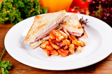 Breakfast toasted sandwiches with cheese and ham, baked beans and sausages on white plate