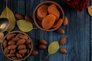 Autumn arrangement with almond dried apricots and a warm scarf and yellow leaves on a dark blue wooden table. top view