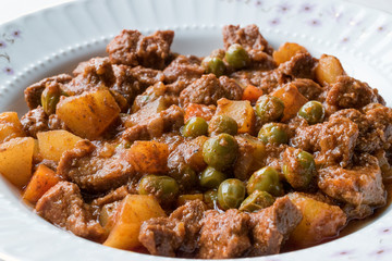 Turkish traditional tas kebab with potato, pea and tomato in a white plate