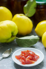 Quince jam on a white saucer, quince fruits and jars of jam on a gray background.