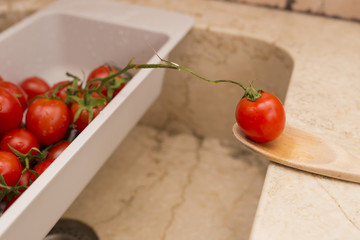 image of cherry tomatoes in plastic container and wooden spoon with tomato sauce
