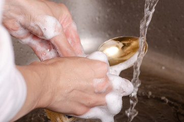Sponge for washing utensils a spoon in the hands of a kitchen sink faucet water