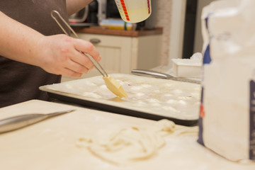 horizontal image with detail of woman's hands using kitchen brush to smear oil during the preparation of the focaccia