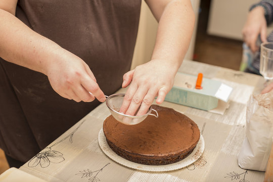 horizontal image of woman's hands dusted cocoa over chocolate cake
