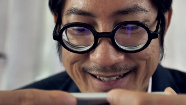 Close up of Asian bearded man using his phone with smile face, 4K slow motion of asian man wearing eyeglass watching on mobile phone.