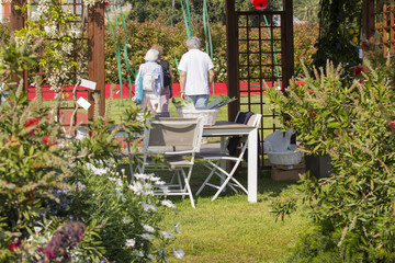 horizontal image of wooden garden furniture under a gazebo with people strolling and resting