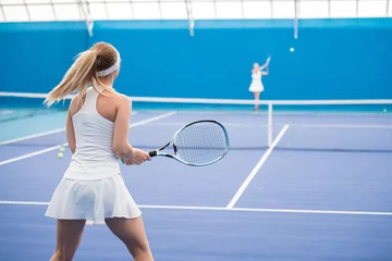 Rolgordijnen Back view portrait of female tennis player holding racket during training in indoor court, copy space © Seventyfour