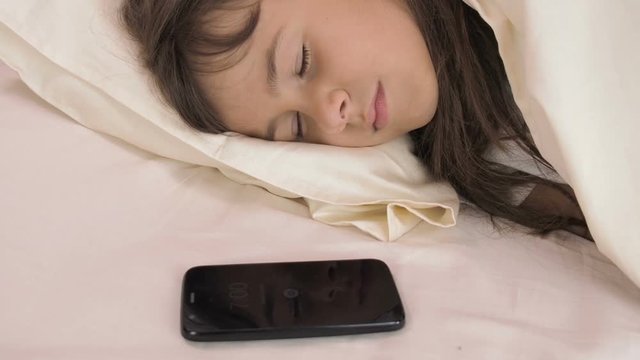 Alarm clock on the phone. The girl is sleeping in the bedroom with the alarm on the phone.