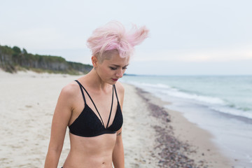 beautiful young sexy woman model, girl with trendy, stylish haircut, pink hair and 
shaved temples and tattoo, dressed black lingerie. Punk/hipster girl posing on the beach