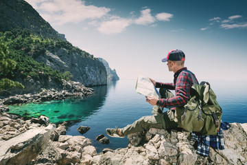 Tourist with a map in the mountains by the sea travels the wilderness. Adventures of a man with a backpack on the island. The hiker relaxes. Young backpacker.