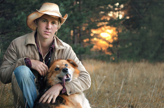 young man in a cowboy suit hugs his dog sitting on vacation at the edge of the forest