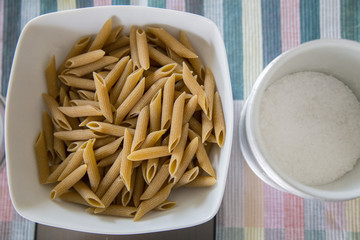horizontal image with top view of a plate of wholemeal pasta on digital scale with jar of salt