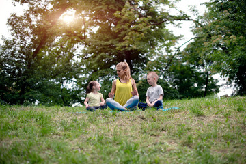 Obraz premium Young family of mother and children son and daughter are engaged in fitness, yoga, exercise in the park. Healthy sport lifestyle concept