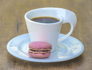Beautiful white cup of black coffee and pink french macaroon on wooden table