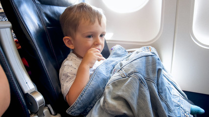 Little toddler boy sitting in airplane seat and having snack