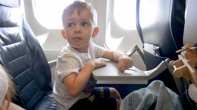 Little Boy Being Scared During Flight In Airplane Looking At Mother