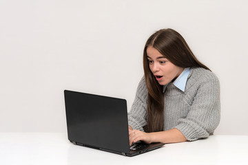 Naklejka premium Portrait of a beautiful teen girl on a white background sitting at a table with a laptop.