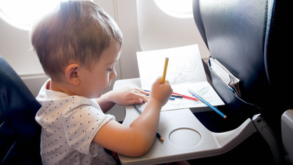 Obraz premium Toned portrait of little toddler boy traveling by plane and drawing with pencils during long flight