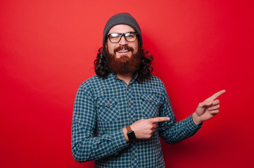 Portrait of smiling young bearded man pointing away over red background