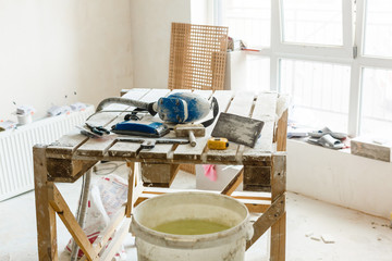 Construction grunge ladder, paint roller and paint bucket in white interior: white wall and gray floor. Apartment decoration concept.