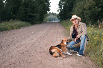 guy in a cowboy hat hugs his dog on a country road