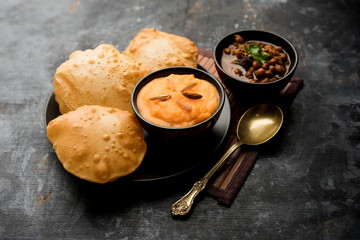 Suji/Sooji Halwa Puri or Shira Poori with black chana masala breakfast, served in a plate and bowl. selective focus
