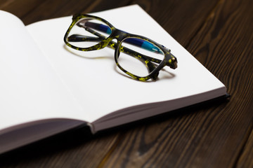 Open blank book, pen and glasses on dark wooden table. View from above. Space for text. closedup