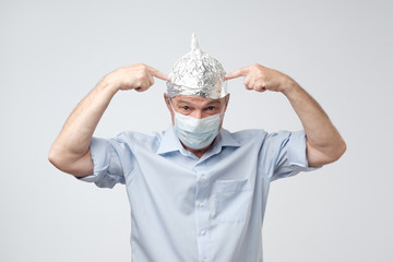 Caucasian mature man in a tin foil hat and medical hat displeased hiding from outdoor life. Afraid...