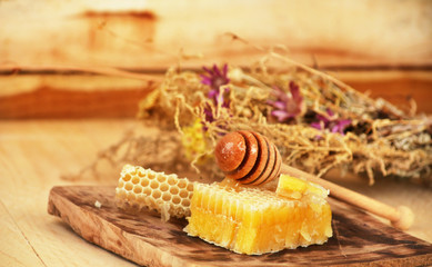 Pieces of honeycomb with wooden stick with honey are on a wooden board.