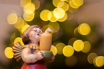 Angel figure as candlestick in front of a Christmas tree with blurred lights.