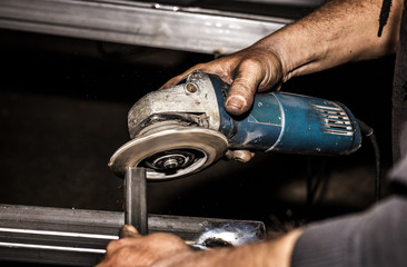 Craftsman sawing metal with disk grinder in workshop. Grinding metal