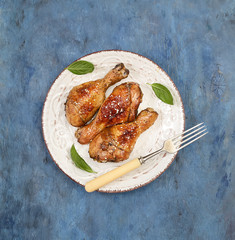 Roasted chicken drumsticks with sesame on a plate on a blue background