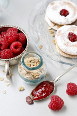 Spoon with raspberry jam, jar of muesli, homemade cookies and bowl of ripe fruits.