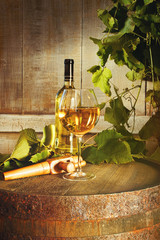 Closeup of bottle of white wine with glass on barrel