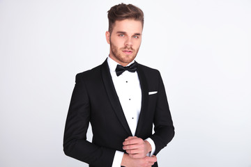 portrait of young man in black tuxedo fixing his links