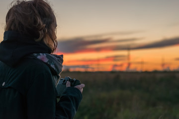 Young lady taking photos of beautiful dusk, using antiques film camera