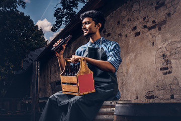 Brewmaster sitting on a wooden barrel and holds a glass of craft beer, relaxes after work.